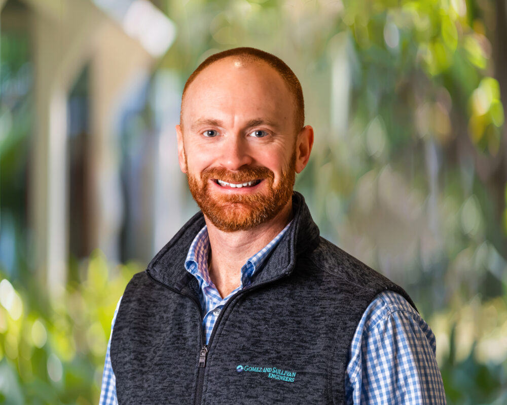 Headshot image of Tim Sullivan in a blue button down shirt and vest against an outdoor background